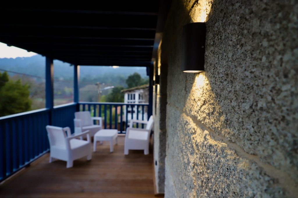 Terraza rústica de Casa de Aldea Caneirón. Corredor azul cielo con sillas y mesa blancas, ideal para desconectar viendo los viñedos de O Ribeiro.
