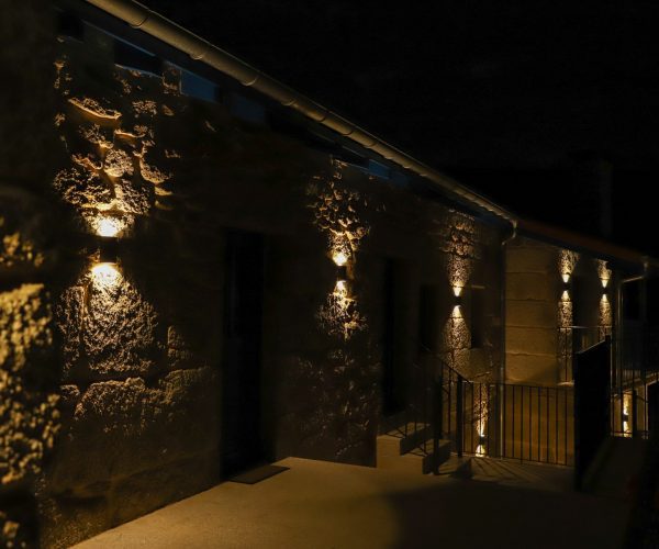 Fachada de piedra de Casa de Aldea Caneirón de noche, iluminada. Una Casa rural en Ourense con piscina que conserva el estilo de una casa rústica en Galicia.